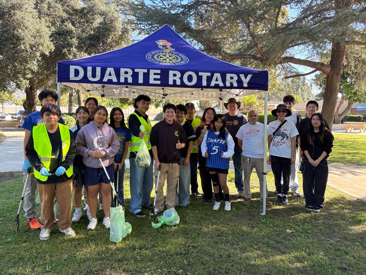 A group of volunteers with cleanup gear stands under a Duarte Rotary tent outdoors.